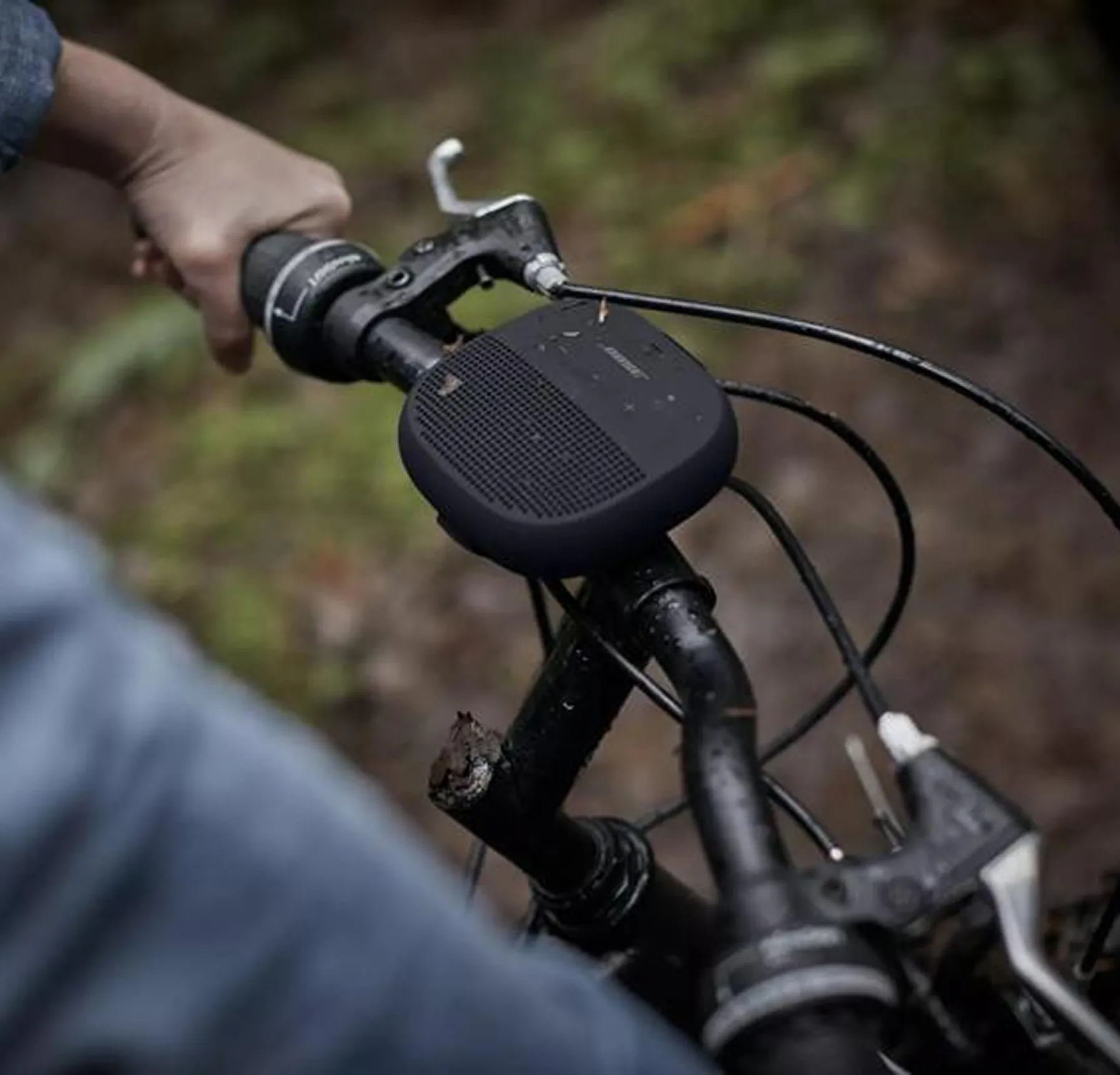 Close-up of a hand holding the handlebar of a bicycle with a black Bose portable speaker mounted on it.